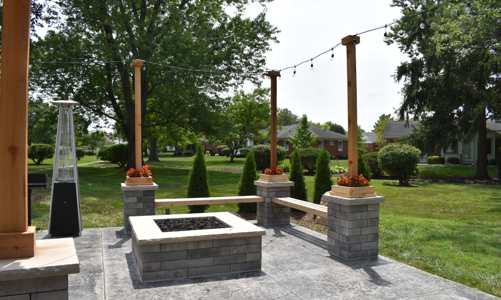Precision Outdoors Greenwood Indiana Smock Courtyard senior living community large pergola arborvitae bubbling boulder water feature fountain propane fire pit seating corner propane heaters heat source custom landscaping flowers mulch night lighting string lights grill propane heaters flowers shared living space exterior design and build perfectly manicured turf